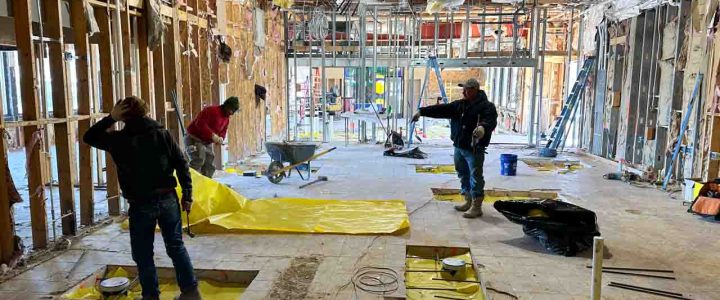 Workers inside a building under construction, using yellow tarps to protect areas during the work process.