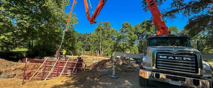 A concrete pump truck with its boom extended, pouring concrete into forms at a residential construction site.