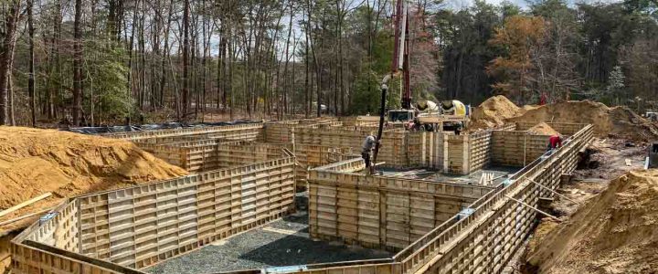 Workers constructing concrete foundations using wooden forms and pouring equipment.