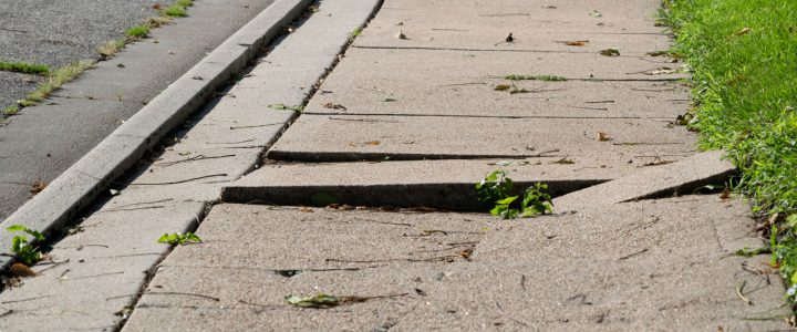 A cracked and uneven concrete sidewalk showing signs of wear and damage.